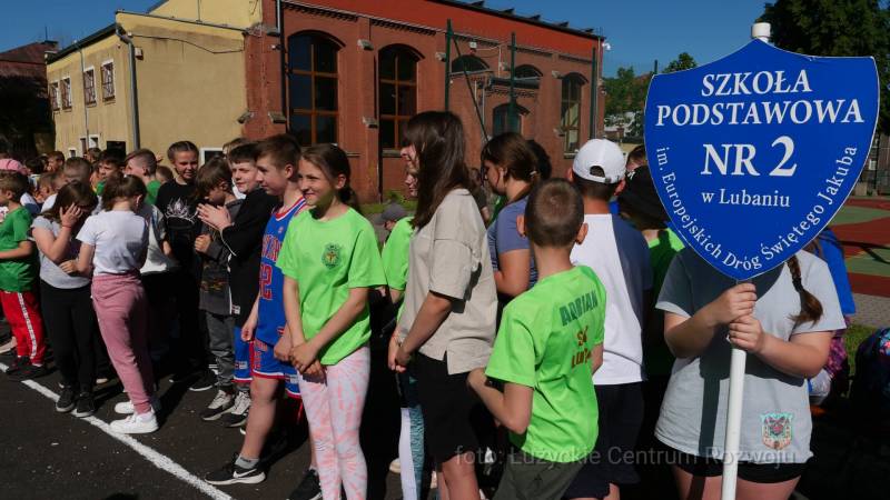 grupa dzieci, jedno trzyma tablicę w kształcie tarczy szkolnej z napisem Szkoła Podstawowa nr 2 w Lubaniu